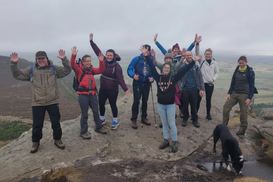 Group of people and a dog posing on a rocky outcrop with a scenic landscape in the background.